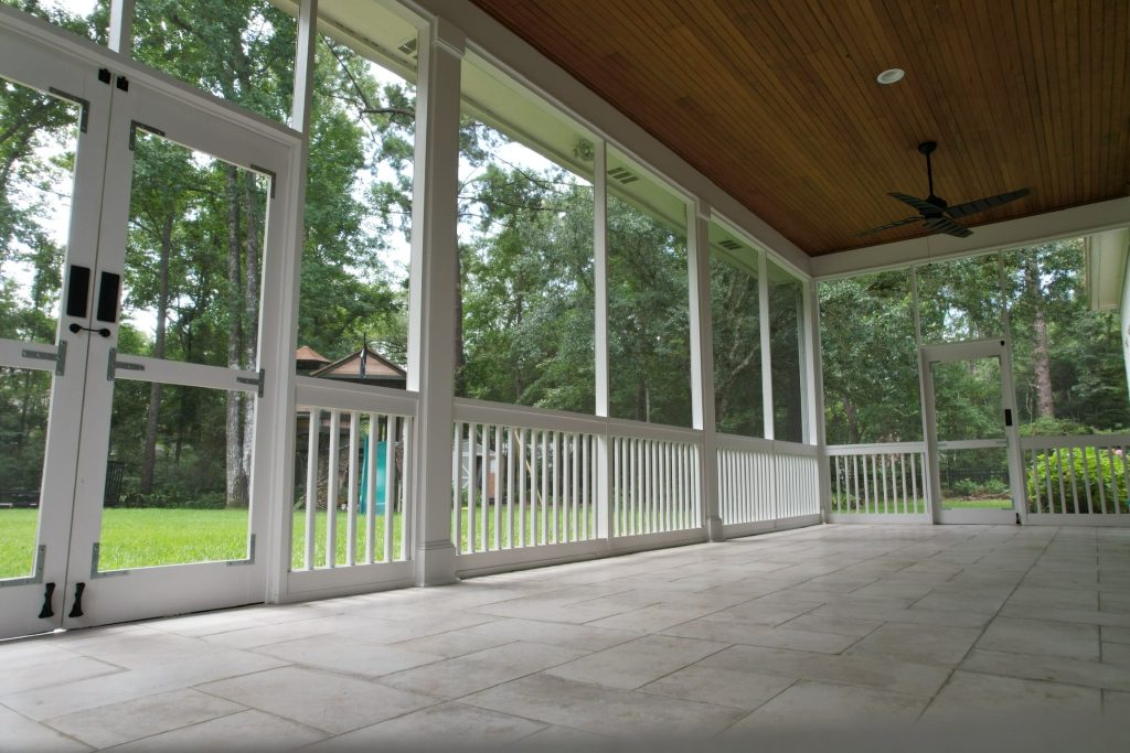Custom screened-in porch installation in Covington, Louisiana featuring white framing, wood tongue-and-groove ceiling, tile flooring, and ceiling fan.