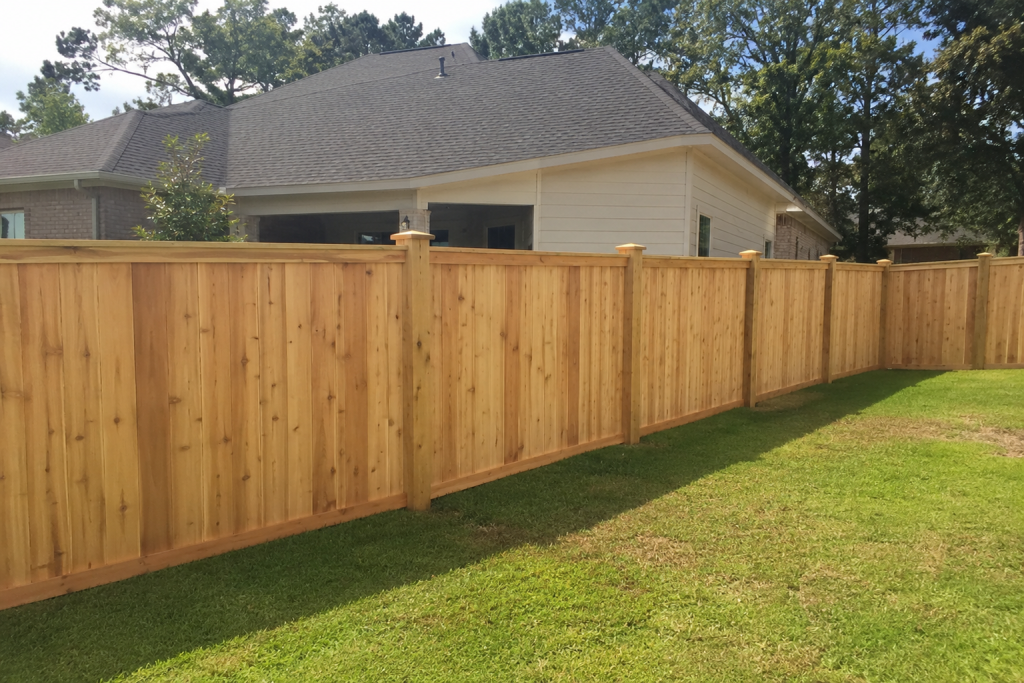 Custom cedar privacy fence installation with decorative top cap posts in a new construction backyard in Covington, Louisiana.