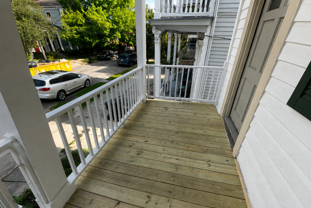 Newly rebuilt second-story pressure-treated pine balcony deck with white railings on a historic New Orleans multi-family home.