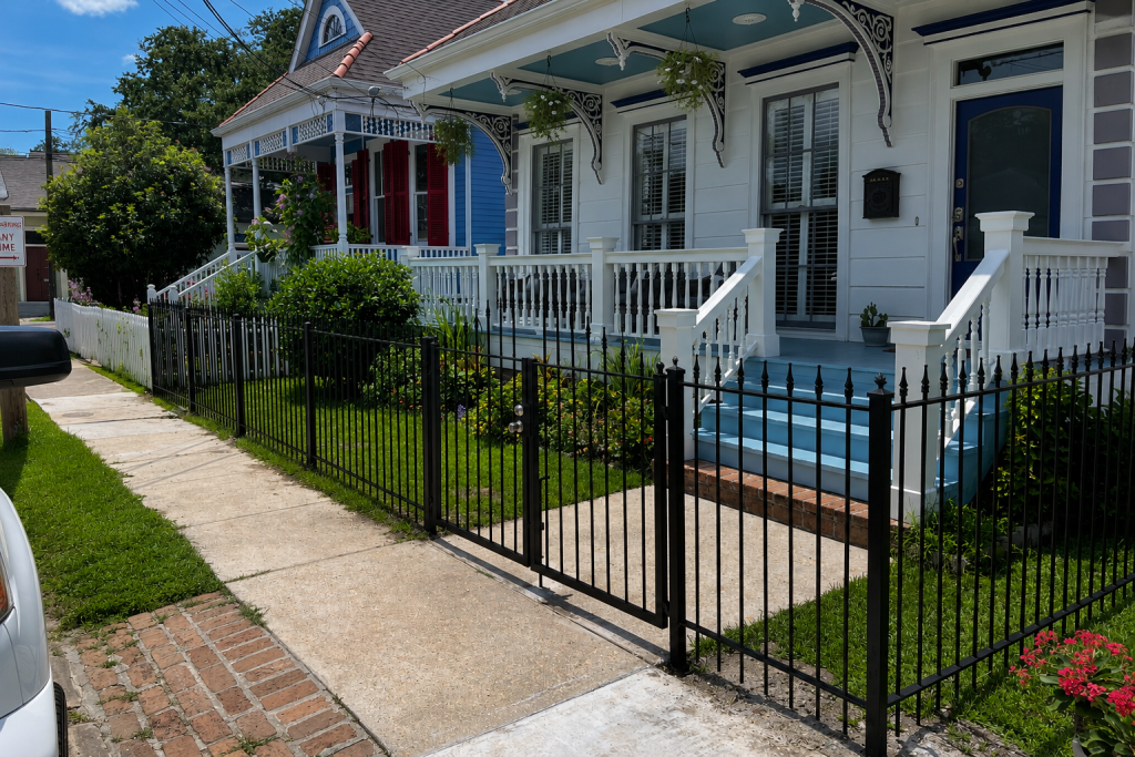 Black ornamental aluminum front yard fence and gate installed in front of a historic New Orleans home with decorative porch details.